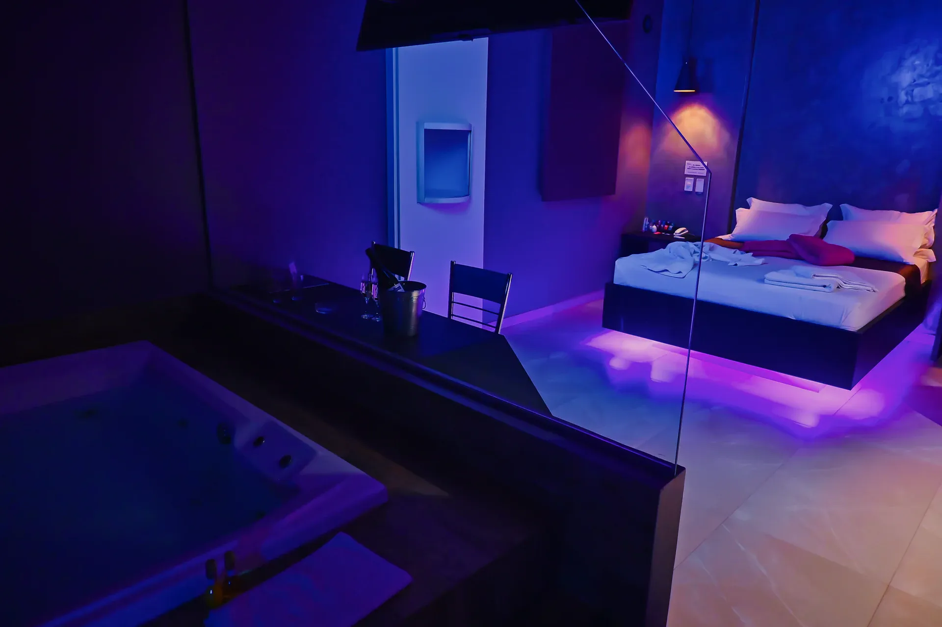 Cama e banheira de hidromassagem da Suíte Hidro Plus sob luz azul e violeta