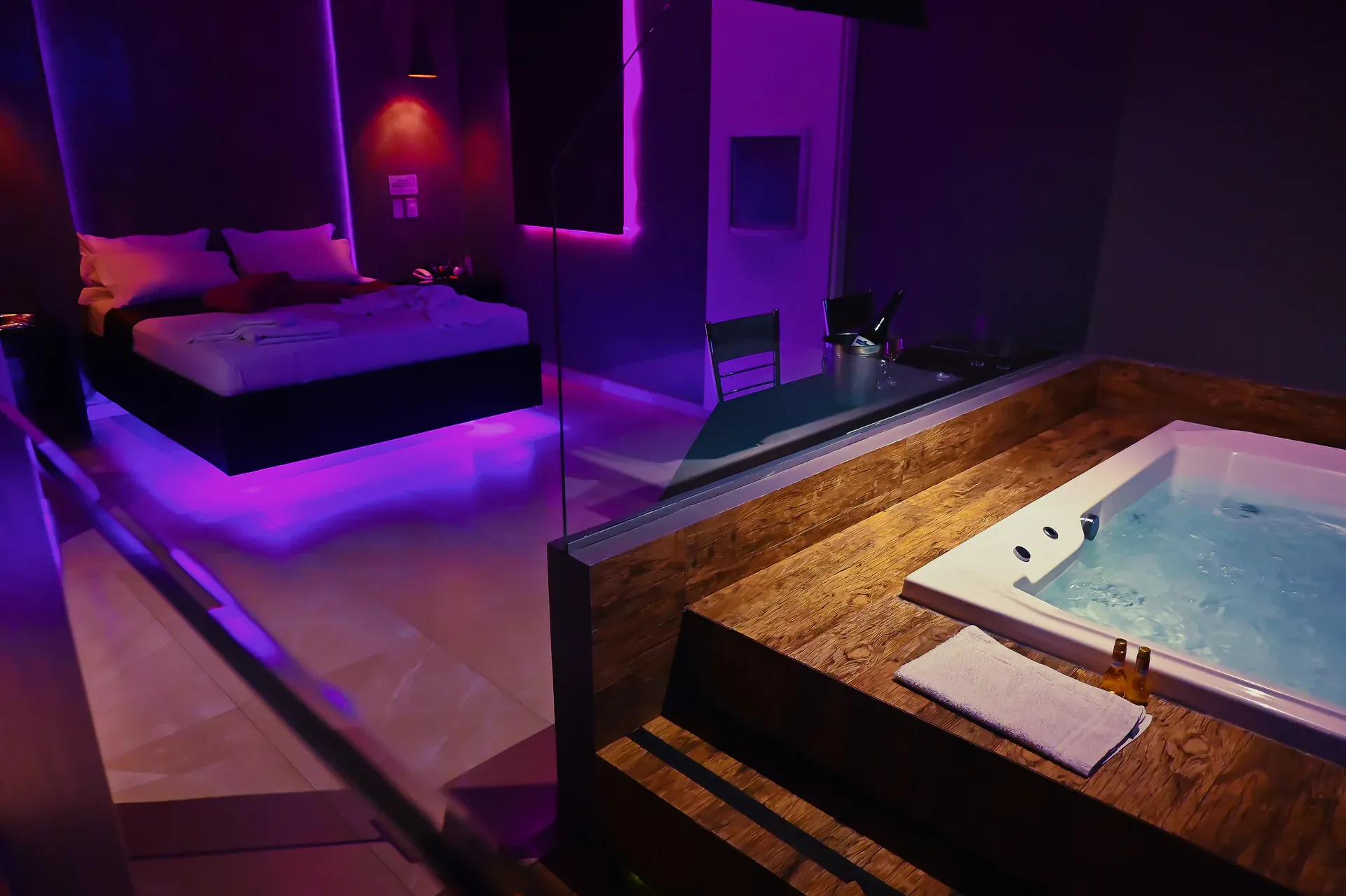 Banheira de hidromassagem com água borbulhando e cama iluminada ao fundo