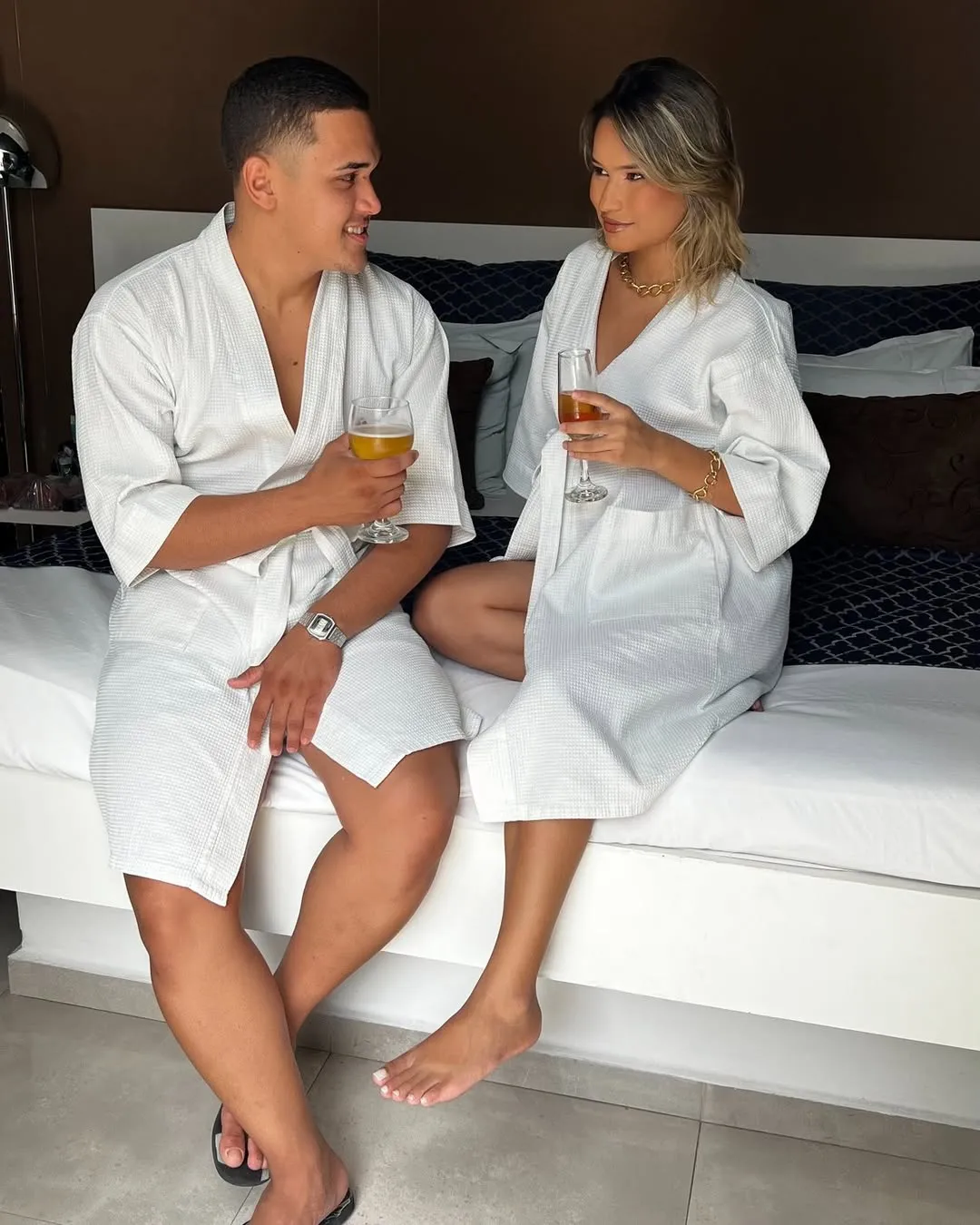 Casal de roupões sentado na cama de uma suíte do Motel Opium