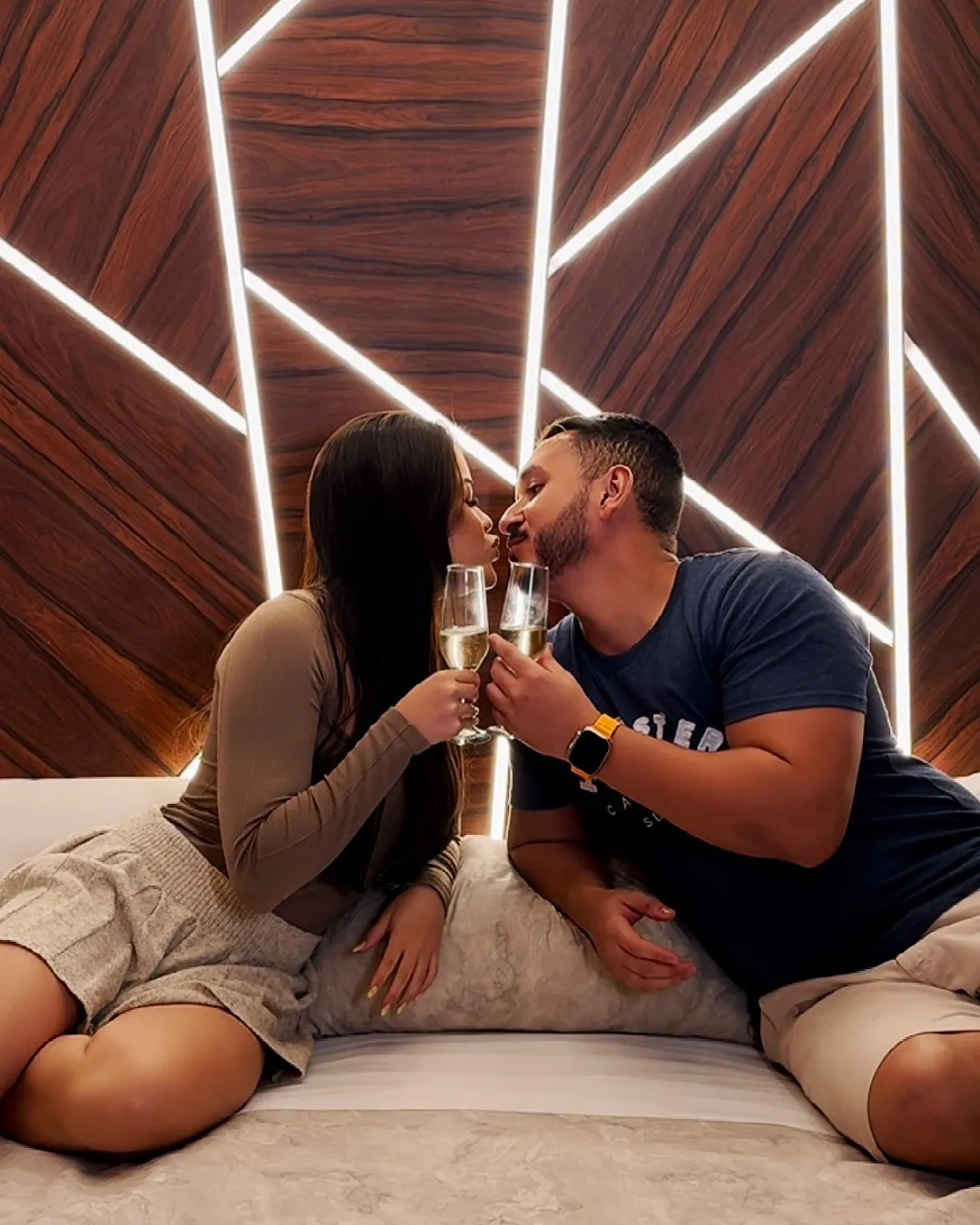 Casal brindando com taças de espumante sentado na cama