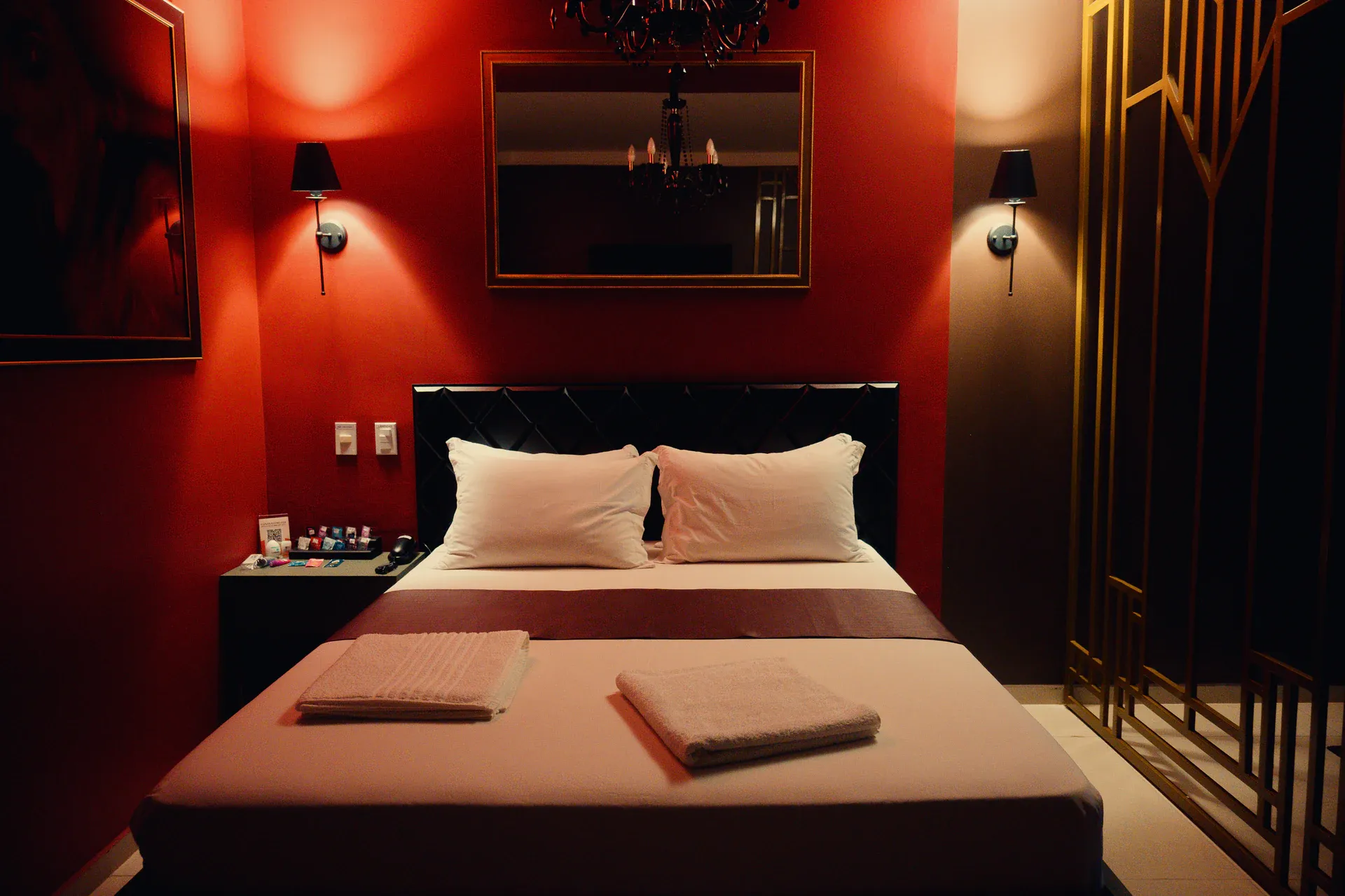 Cama da Suíte Luxo diante de parede vermelha, espelho e lustre preto