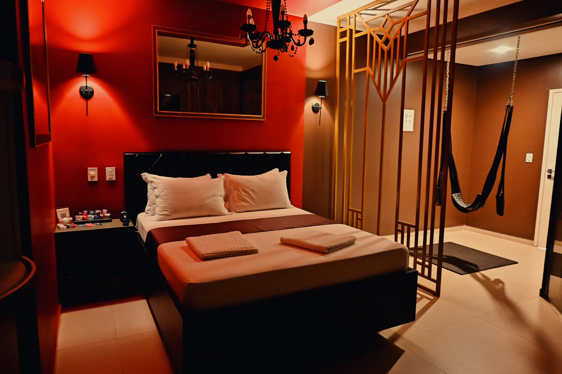 Suíte Luxo vermelha com cama, lustre e balanço atrás da divisória dourada