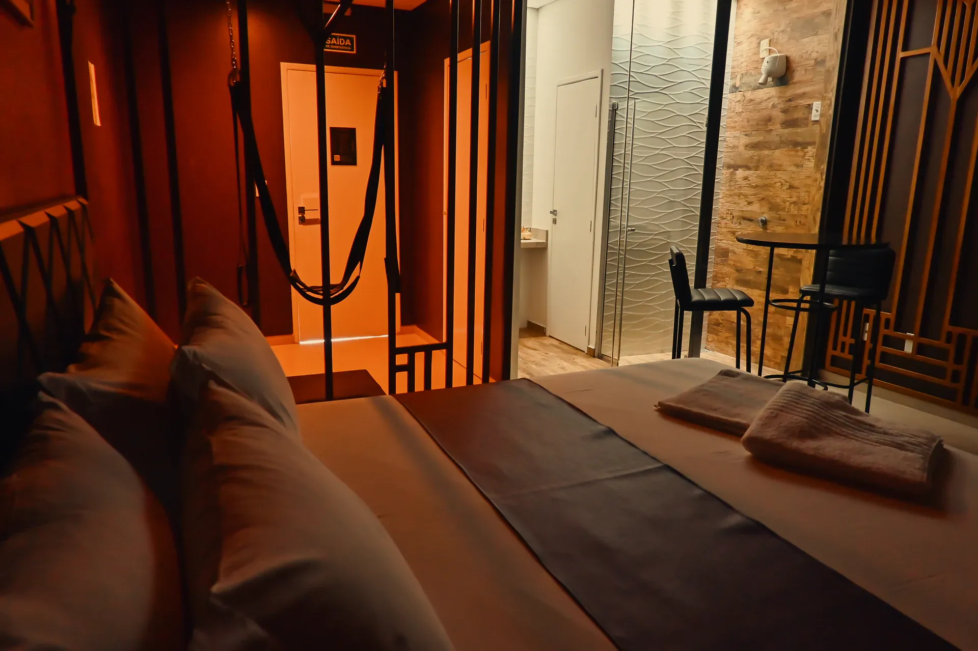 Cama com balanço suspenso, box de vidro e mesa alta ao fundo