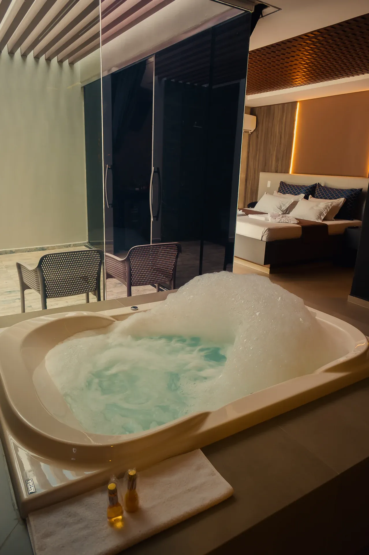 Hidromassagem com espuma em primeiro plano e cama iluminada ao fundo