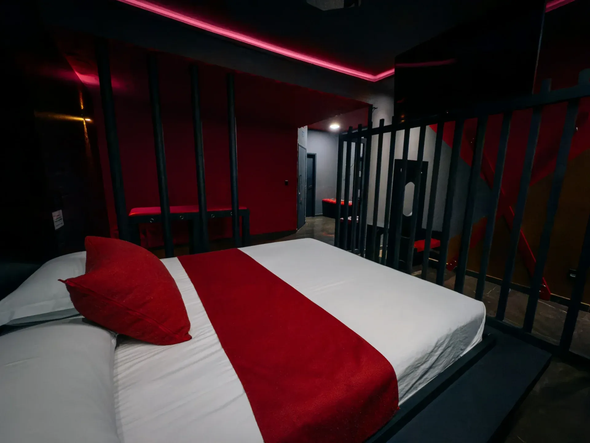 Suíte Sado vista através da divisória, com cama e iluminação vermelha