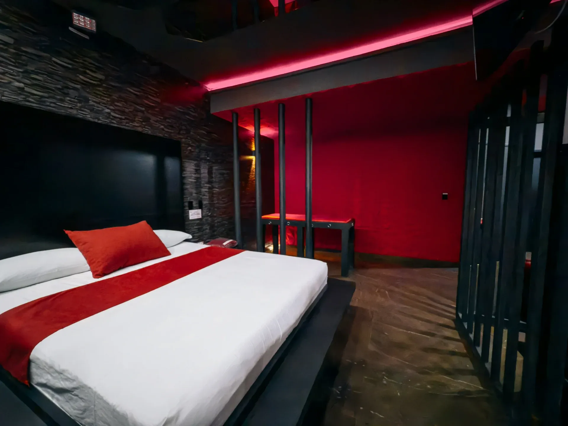 Cama da Suíte Sado diante de parede geométrica em tons de vermelho e preto