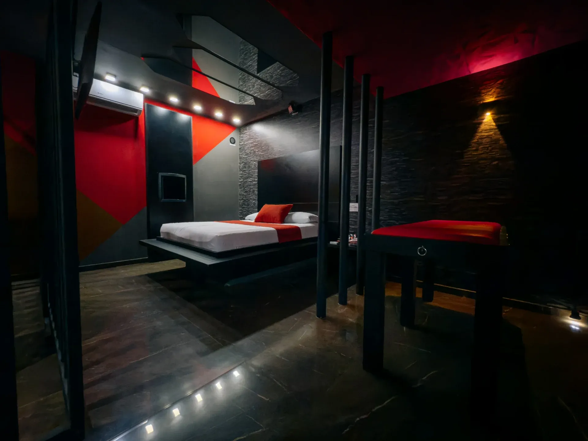 Visão ampla da Suíte Sado com cama, parede geométrica e iluminação baixa